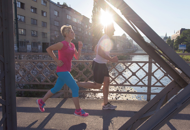 healthy mature couple jogging in the city  at early morning with sunrise in background - Zdjęcie, obraz