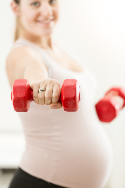 Closeup of pregnant woman's hand holding red barbell - Foto, imagen