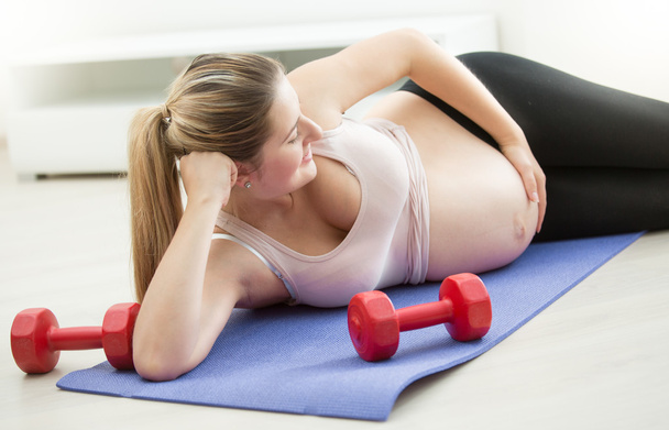 妊娠中の女性フィットネス マットの上に横たわると、大きな腹に触れる - 写真・画像
