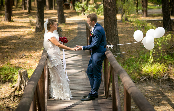 Casado casal posando na velha ponte de madeira com balão branco
 - Foto, Imagem