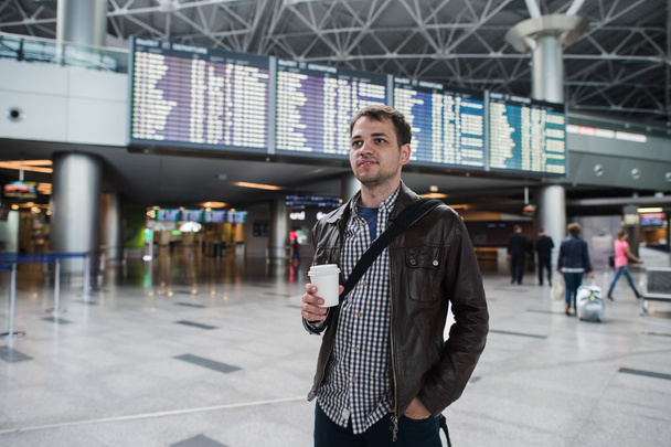Joven viajero con taza de café en el aeropuerto a bordo de salidas y llegadas
 - Foto, imagen