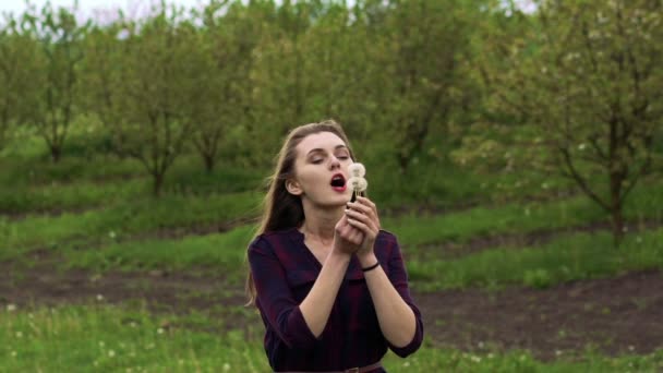 Happy girl blowing the dandelion in the garden. Slow motion - Felvétel, videó