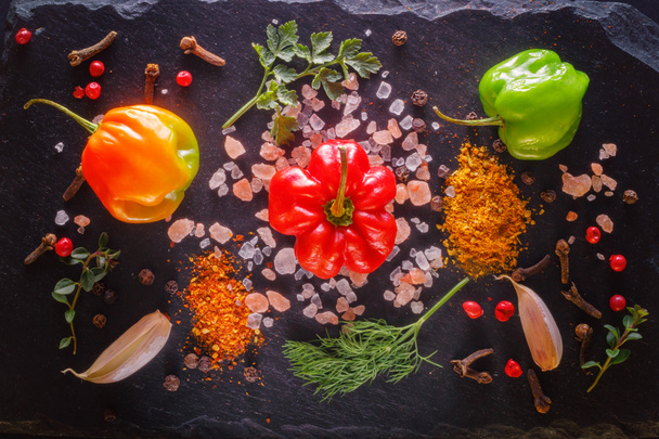 fresh peppers of different colors with pink salt, garlic, ground spices, dill, parsley, thyme on the stone. burning spices. Background  view from above. picture with vintage processing in low key - Φωτογραφία, εικόνα