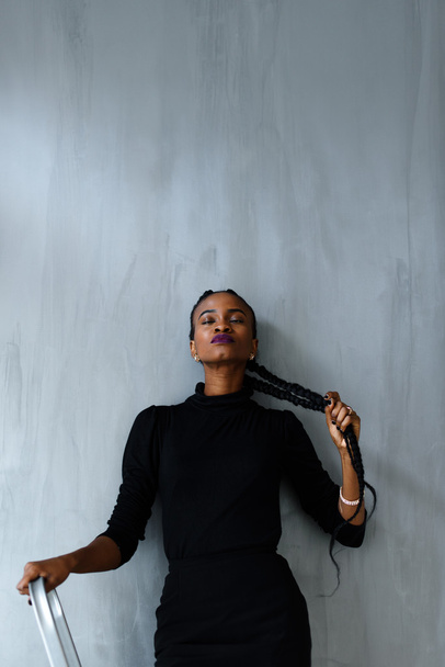 Young pretty black american woman touching her thick plait on dark studio background - Zdjęcie, obraz