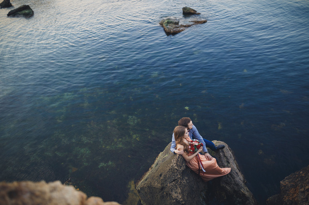 Wedding couple kissing and hugging on rocks near blue sea - Фото, зображення
