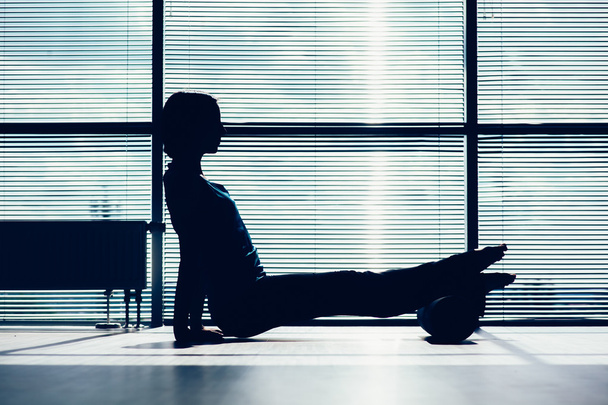 fitness, sport, training and lifestyle concept - woman doing pilates on the floor with foam roller contour of the body against the window - Foto, immagini