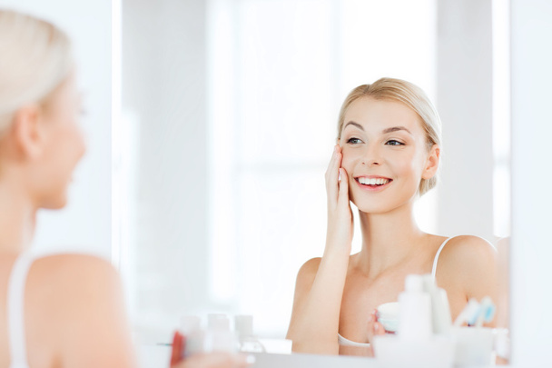 happy woman applying cream to face at bathroom - Foto, imagen