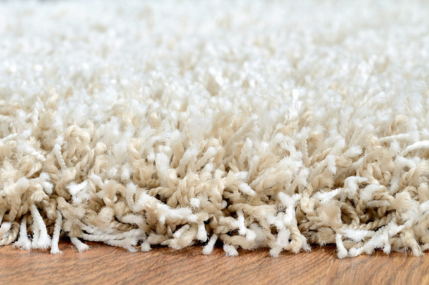 Detail bílých shaggy koberce na hnědé dřevěné podlahy - Fotografie, Obrázek
