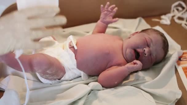 Krankenschwester in Handschuhen setzt weiße Mütze auf dem Kopf des Neugeborenen in der Geburtsklinik auf. Kind weint. - Filmmaterial, Video