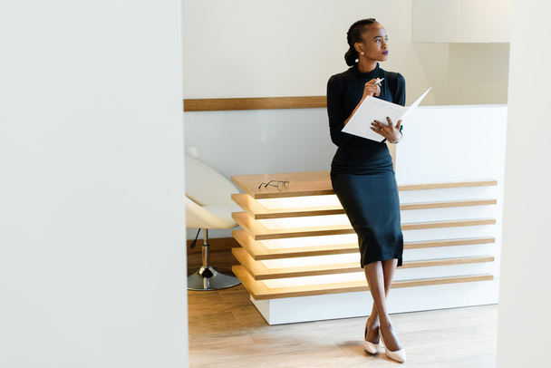 Stern elegant business woman wearing black dress and beige shoes in light office looking towards with her agenda, full length portrait - Fotoğraf, Görsel