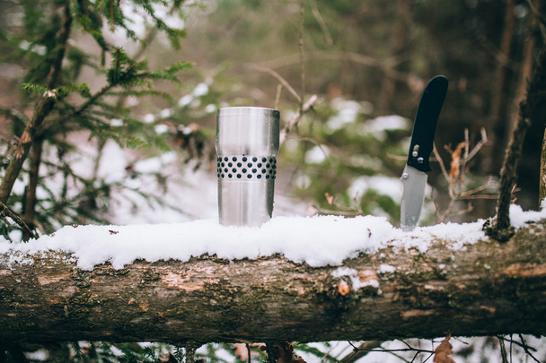 Thermoss und Taschenmesser auf einem schneebedeckten Holz  - Foto, Bild