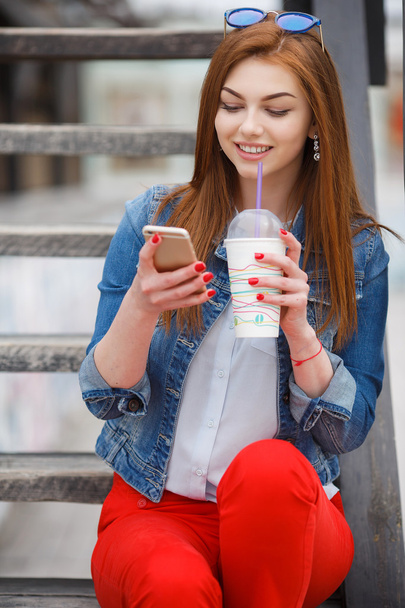 Young woman with a cocktail , reading a text message on the street - Photo, image