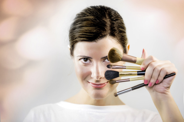 mooie jonge vrouw met make-up borstels in hand op witte achtergrond - Foto, afbeelding