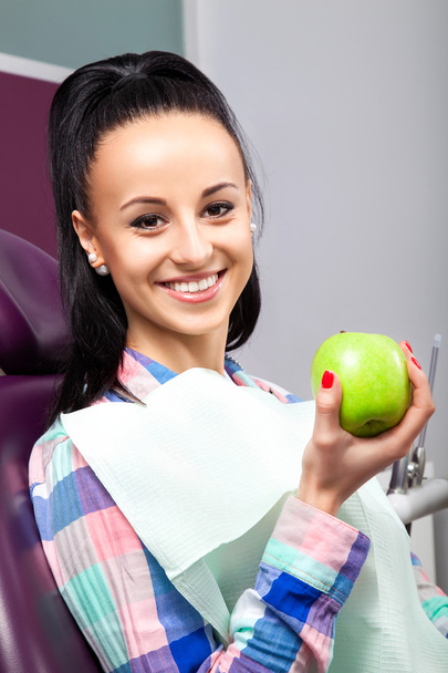 Beautiful woman patient in dental chair smiling with green apple - Foto, Bild
