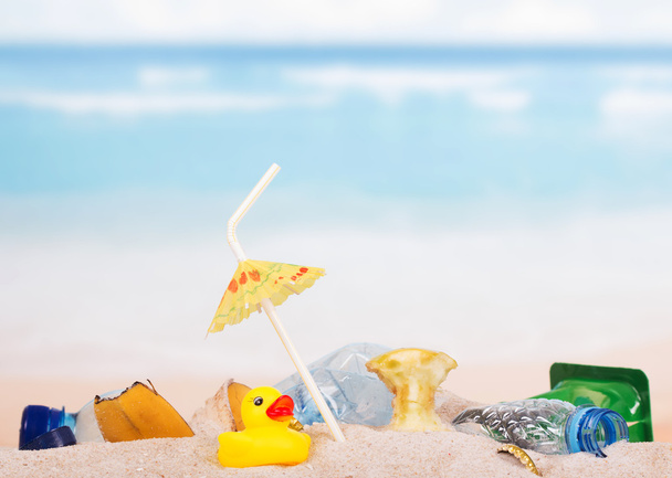 Residuos domésticos, sobras y pato de goma en arena contra el mar
. - Foto, Imagen