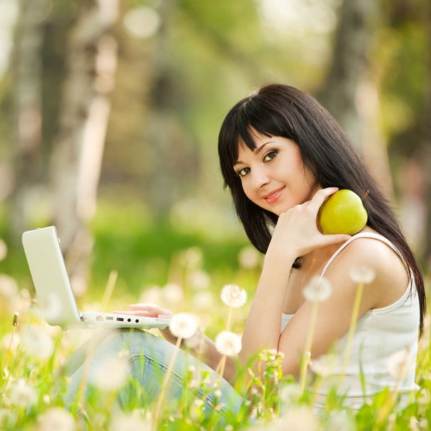 Femme mignonne avec ordinateur portable blanc dans le parc avec des pissenlits
 - Photo, image