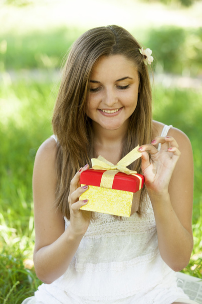 Красива дівчина-підліток з подарунком в парку на зеленій траві
. - Фото, зображення