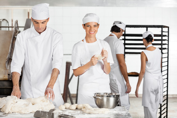 Female Baker Kneading Dough With Colleague In Bakery - Foto, Imagen