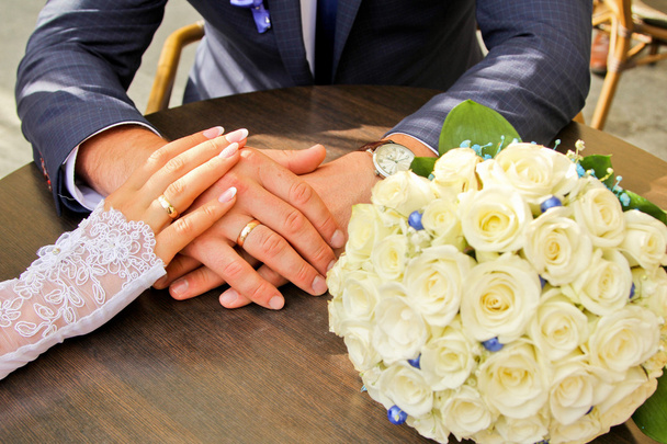 Τα χέρια και τα δαχτυλίδια. άσπρα Γαμήλια ανθοδέσμη στο τραπέζι από ξύλο - Φωτογραφία, εικόνα