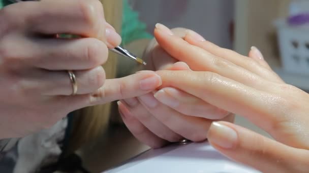 Специалист по ногтям делает клиенту маникюр в маникюре. Молодая женщина получает французский маникюр
. - Кадры, видео