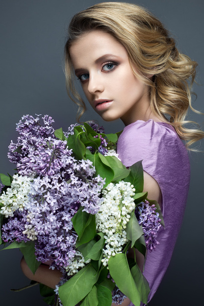 Beautiful girl in a purple dress and a bouquet of lilacs. The model is in an image of spring. - Photo, image
