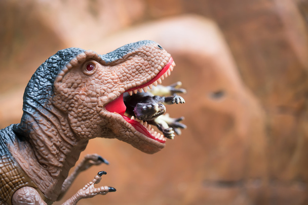 гигантский тираннозавр ловит маленького динозавра перед скальной горой
 - Фото, изображение