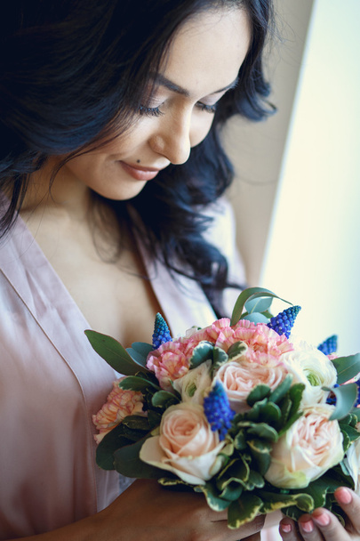 Close-up portrait of beautiful brunette bride before wedding, holding bridal bouquet in a morning - Фото, изображение