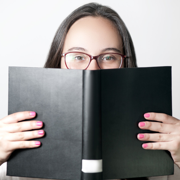 Nahaufnahme Porträt einer lächelnden jungen Frau mit Brille, die ein großes schwarzes Buch liest - Lernkonzept - Foto, Bild