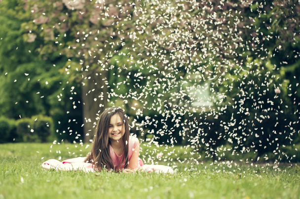 Little girl on green grass with petals - Фото, зображення