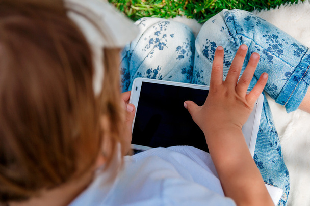 Little baby girl dressed in white polo and jeans.Girl Using a Tablet. Little girl studies with the tablet - Foto, imagen