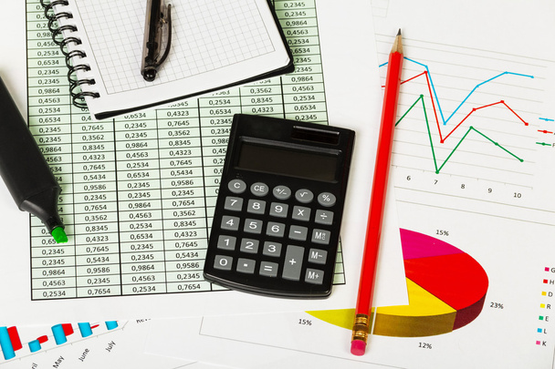 Jegyzettömb, toll, marker, ceruza és számológép, háttérben a grafikonok. - Fotó, kép