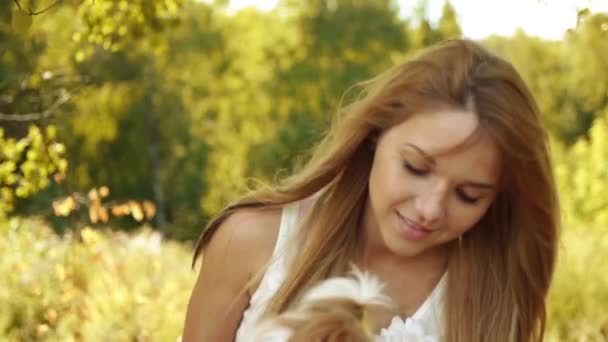 Retrato de mulher sorridente muito jovem segurando pequeno cachorro fofo, contra o fundo do parque verde de verão
 - Filmagem, Vídeo