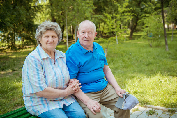 Senior couple sitting on a park bench with walking stick. Elderly couple relaxing outdoors on a summer day. - Foto, Imagem