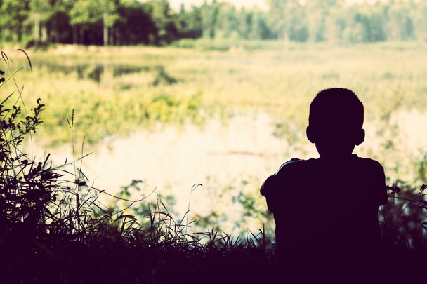 Smutny chłopiec siedzący obok rzeki. - Zdjęcie, obraz
