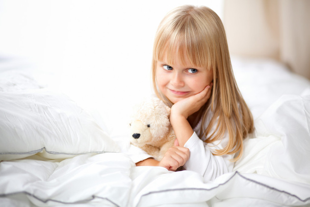 Little girl with teddy bear lying on the bed at home - Foto, imagen