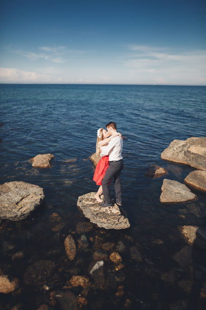 Ρομαντικό ζευγάρι ερωτευμένων που παρουσιάζουν στις πέτρες κοντά στη θάλασσα, μπλε ουρανό - Φωτογραφία, εικόνα