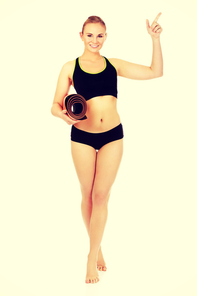 Young athletic woman holding mat and pointing for something - Fotoğraf, Görsel