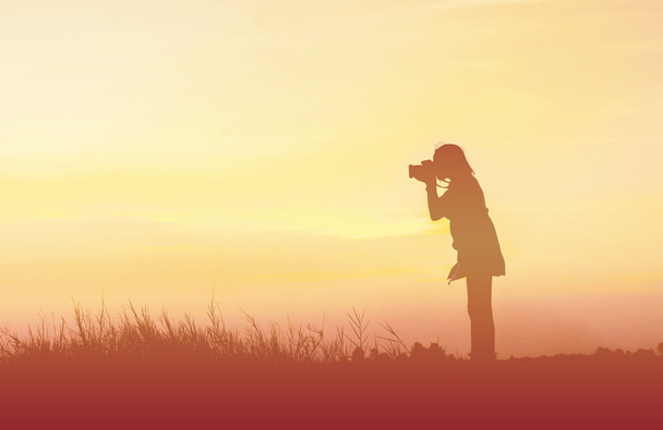 Silhouet vrouw fotograaf bij zonsondergang - Foto, afbeelding