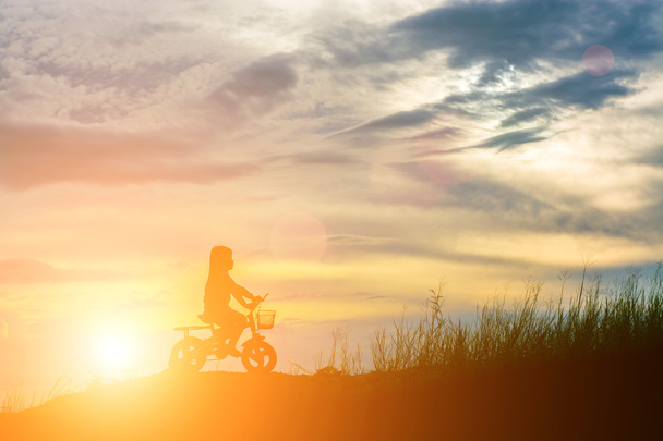 silhouet van klein meisje met kleine fiets op de berg - Foto, afbeelding