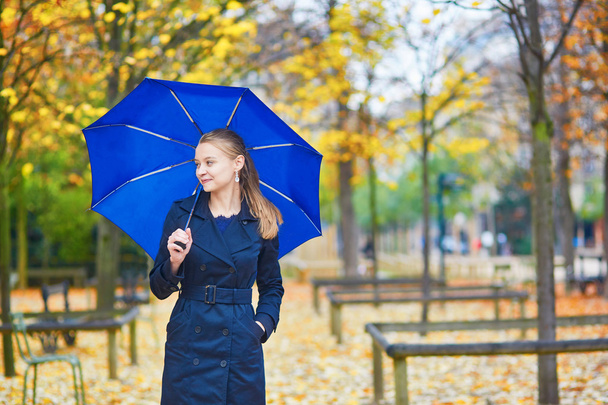 Young woman with blue umbrella in the Luxembourg garden of Paris on a fall or spring rainy day - Photo, Image