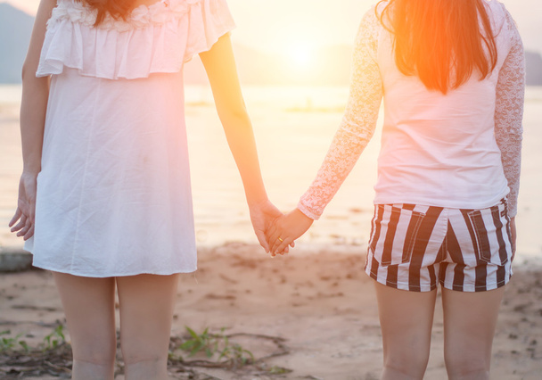 2 人の若い女性は、海辺に一緒に手をつないでください。 - 写真・画像
