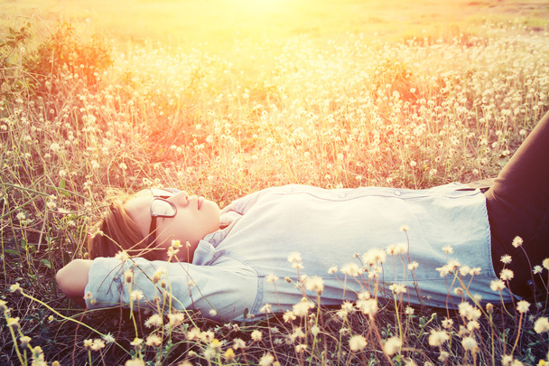 Happy hipster woman lying down on dandelion field close her eyes - Photo, Image