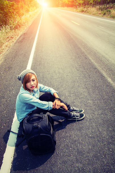 座っている若い女性運ぶヒッチハイクしているバックパックの背面図 - 写真・画像
