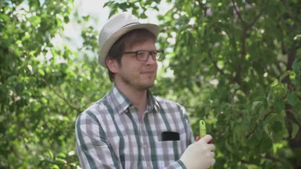 egy fiatal férfi farmer gazdaság rake, és mosolyogva a kertben - Felvétel, videó
