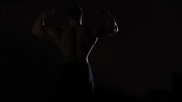 Strong man demonstrating perfect muscular body, male silhouette in darkness - Felvétel, videó