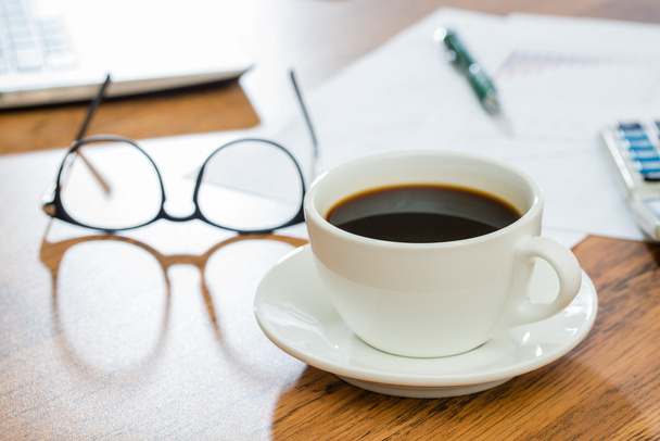 Чашка кави та канцелярського приладдя на дерев'яному столі
 - Фото, зображення
