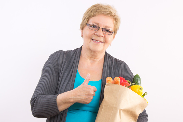 Senior woman holding shopping bag and showing thumbs up, healthy nutrition in old age - Foto, imagen