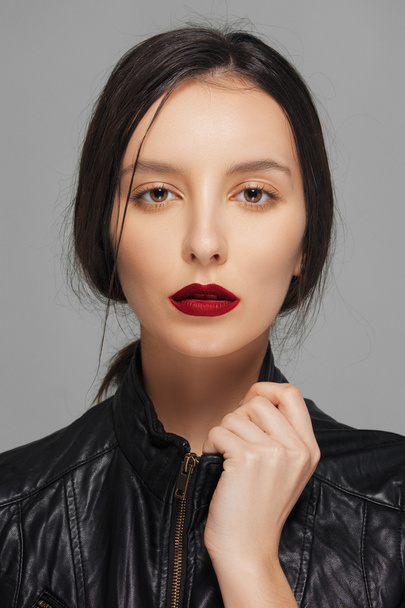 Charming girl in leather jacket touching collar. Red mat lips. - Photo, image