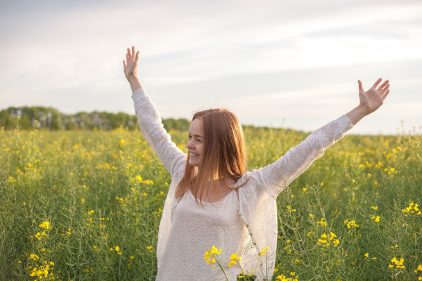 mujer con los brazos abiertos en el campo de colza verde por la mañana
 - Foto, imagen