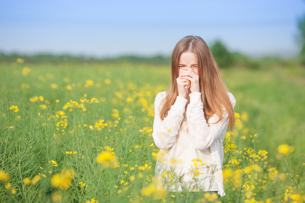 Αλλεργία στη γύρη, φτάρνισμα κοριτσιού σε ένα λιβάδι με λουλούδια. - Φωτογραφία, εικόνα